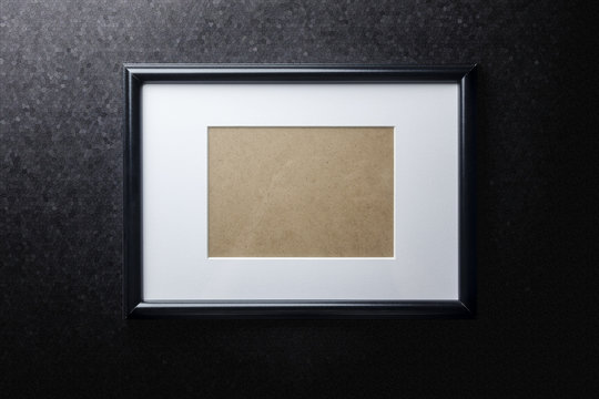 Black plain empty thin wood picture frame with white mat passe-partout on black rough paint wall background