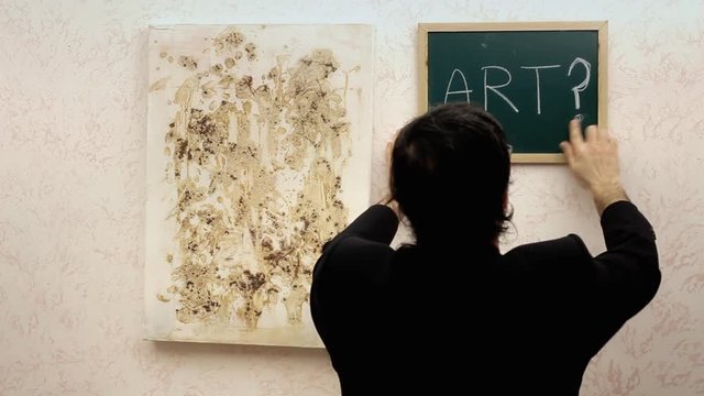 A critic at an art exhibition, putting a frame with the word "Art?" near an abstract painting.