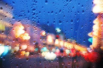 Drops of rain on blue glass with urban defocused lights