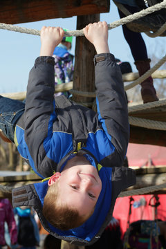 Junge hängt kopfüber am Klettergerüst, Spielplatz
