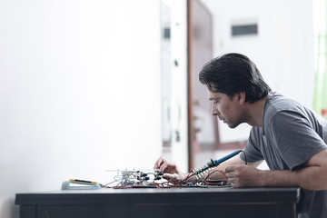 Young man making an electronic device soldering and adjusting the components