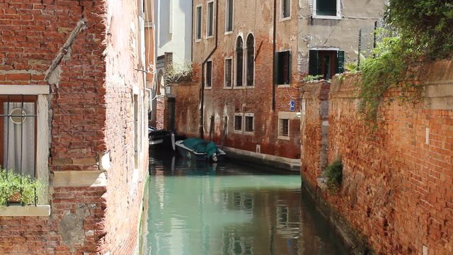 Canal between red houses in Venice, Italy. Sunshine and shadow. Boat laying in water.