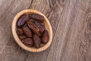 Dried dates in a wooden bowl on a wooden background