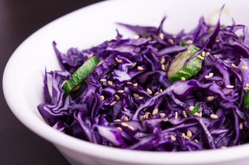 Purple cabbage slaw with sesame seeds, in a white bowl dark background, close up