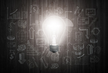 Glowing light bulb on wooden wall with drawing charts and graphs about business success strategy plan