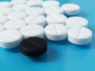 a black tablet pill in front of scattered white ones, cure, medicine, doping, shallow depth of field