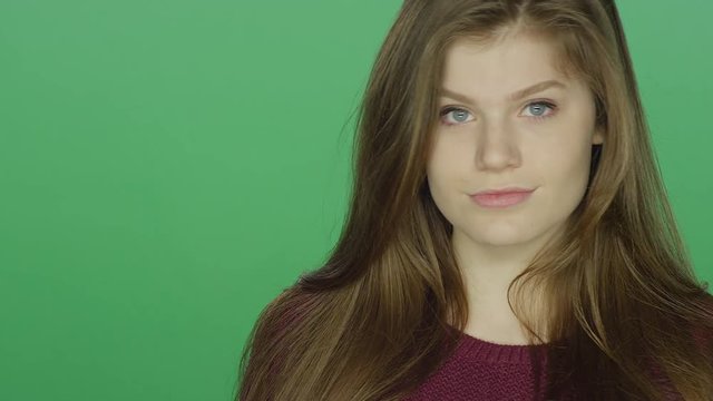 Young brunette woman posing and grinning, on a green screen studio background