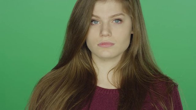 Young brunette woman blankly staring, on a green screen studio background 