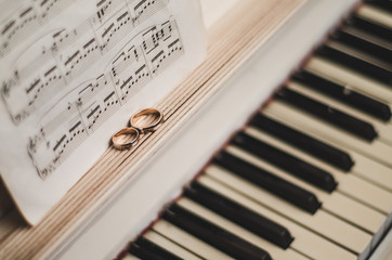 Pair golden rings on classic, piano keyboard with music notes. Wedding accessories. Black and white background, selective focus 