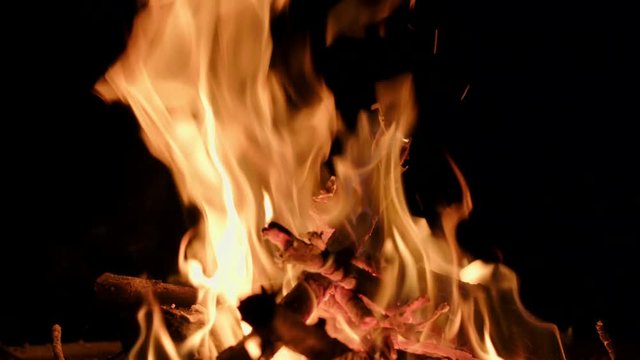 Wood burning and flames rising up from a back-yard fire pit at night.  Slow motion, recorded in 4K at 60fps.