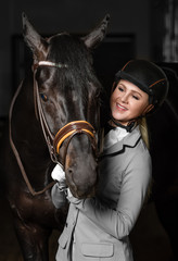 Horsewoman in uniform with a brown horse in the stable.