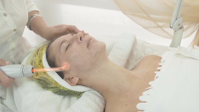 Cosmetologist make  darsonvalization on woman face and neck in beauty saloon. Skincare. Cosmetic procedure. Close up
