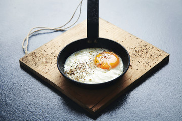 Close view tasty healthy breakfast: spiced with pepper fried egg in mini cast iron vintage pan on wooden pad d isolated on vintage rustic table