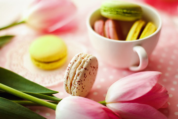 Fototapeta na wymiar A beautiful flowers pink tulips with colorful macaroons laid in cup on white wooden background
