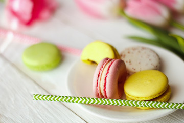 A beautiful flowers pink tulips with colorful macaroons laid on a white platter on white wooden background