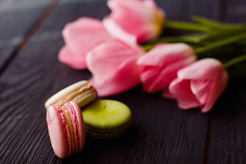 A beautiful flowers pink tulips with colorful macaroons laid on dark wooden background