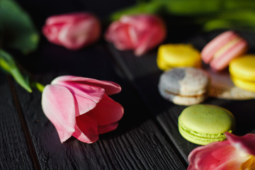 A beautiful flowers pink tulips with colorful macaroons laid on dark wooden background
