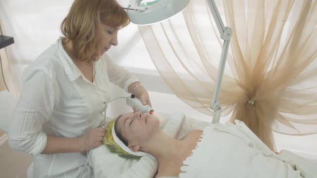 Cosmetologist use darsonval on woman face in beauty saloon. Skincare. Cosmetic procedure. Medium shot
