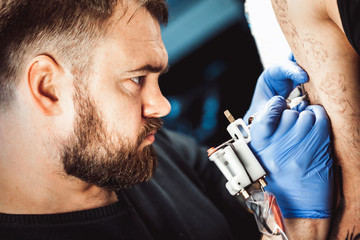 master tattoo artist with a beard makes gloves tattoo on hand men