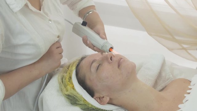 Cosmetologist make  darsonvalization on woman face in beauty saloon. Regeneration of skin. Cosmetic procedure. Medium shot