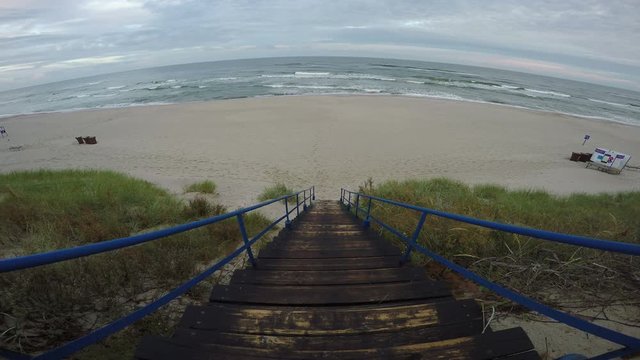 Wooden stairs with blue metal railing to the beach on overcast windy day, 4K