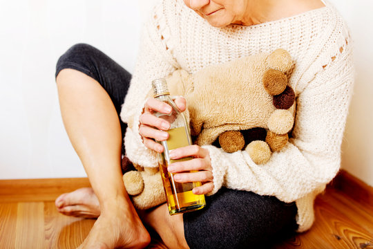 Elderly Sad Woman Sitting In The Corner And Drinking Whiskey