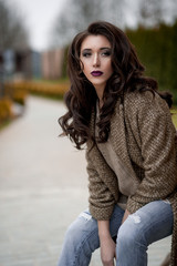 Spring in the country style. Full length portrait of young woman in white knitted sweater and furry hat standing in the front of rustic wood wall in the yard near house, wearing sweater casual.