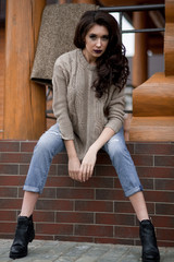 Spring in the country style. Full length portrait of young woman in white knitted sweater and furry hat standing in the front of rustic wood wall in the yard near house, wearing sweater casual.