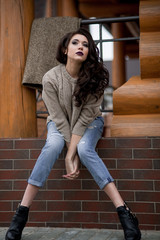 Spring in the country style. Full length portrait of young woman in white knitted sweater and furry hat standing in the front of rustic wood wall in the yard near house, wearing sweater casual.