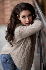 Spring in the country style. Full length portrait of young woman in white knitted sweater and furry hat standing in the front of rustic wood wall in the yard near house, wearing sweater casual.