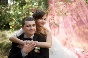 Elegant young happy wedding couple is sitting at green grass on