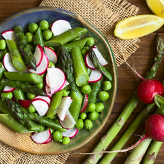 Fresh green asparagus, radish and pea salad served on plate, ingredients on the side, photographed overhead with natural light