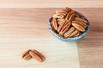 Pecans on wooden surface and in ceramic bowl with copy space. Shallow depth of field.