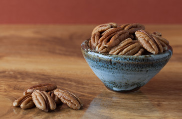 Pecans on wooden table and in ceramic bowl with brown background. Copy space, shallow depth of field