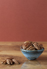 Pecans on wooden table and in ceramic bowl with brown background. Copy space, shallow depth of field