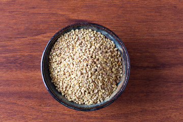 Bee pollen in ceramic bowl on wooden table. Top view with copy space.