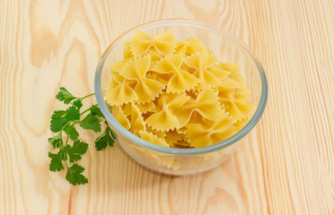 Uncooked bow-tie pasta in glass bowl, sprig of parsley