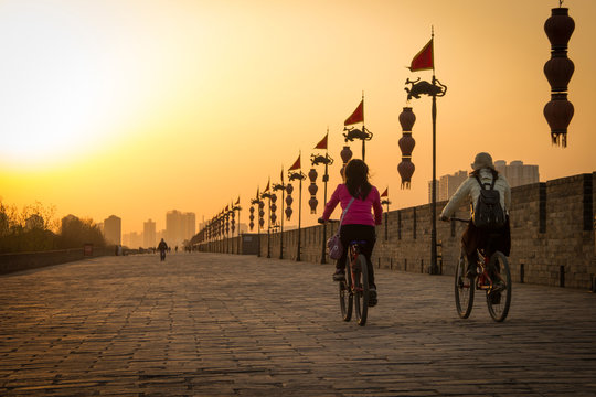 Fototapeta XIAN, CHINA - MARCH 13 2016: People ride bicycle on City Wall of  Xi'an famous Historic Sites in china sunset in the evening