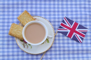 Traditional milky tea served in a bone china cup and saucer with custard cream type biscuits with a Union Jack flag 