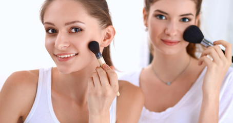 Beautiful girls looking in the mirror and applying cosmetic with a big brush