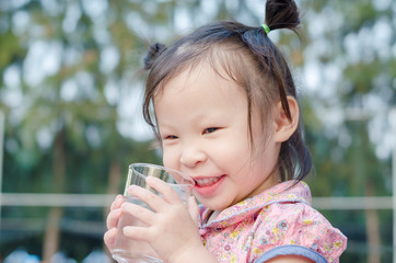 Little Asian girl smiles after drinking water from glass