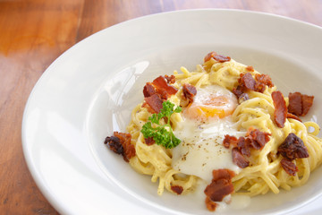 Spaghetti carbonara with crispy bacon and egg on white plate