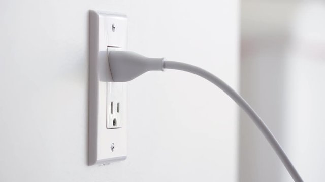Close up of a hand plugging in a power cord and then unplugging it in a typical electrical outlet cover in the USA.  Originally recorded in 4K