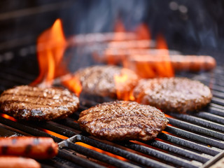 hamburgers and hot dogs cooking on grill with flames - obrazy, fototapety, plakaty