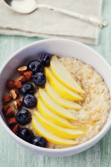 Bowl of oatmeal porridge with apple, berries, honey and almond on rustic table, hot and diet breakfast