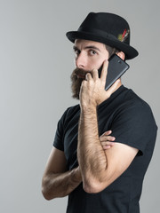Side view of serious bearded hipster talking on the mobile phone looking at camera over gray studio...