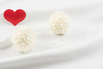 Obraz na płótnie Canvas White chocolate candy coconut truffles and red heart on beautiful white material