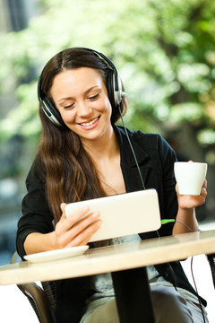 Young woman is using tablet and listening music in cafe.