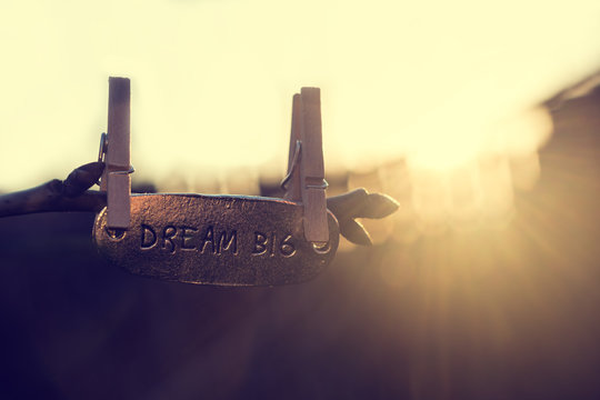 Dream big words written on metallic piece and hanging on a tree branch suspended with small clothes-pin. Beautiful sun shining from behind. Vintage effect applied