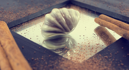 Chocolate praline in seashell form with reflection on wooden background. Vintage effect applied